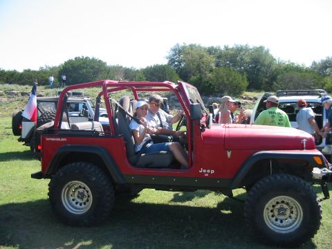 1996 Ford Bronco - Several people gather around off-road vehicles on a sunny day with trees and brush in the background.