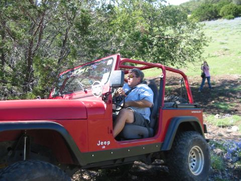 1996 Ford Bronco - A red Jeep Wrangler is driven off-road by a man wearing sunglasses and a blue shirt.