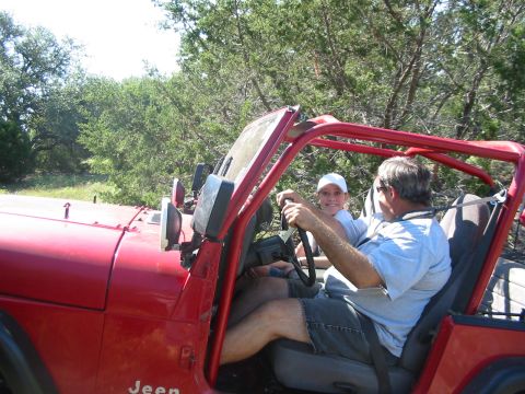 1996 Ford Bronco - Man and child in a red Jeep Wrangler driving through a wooded area.