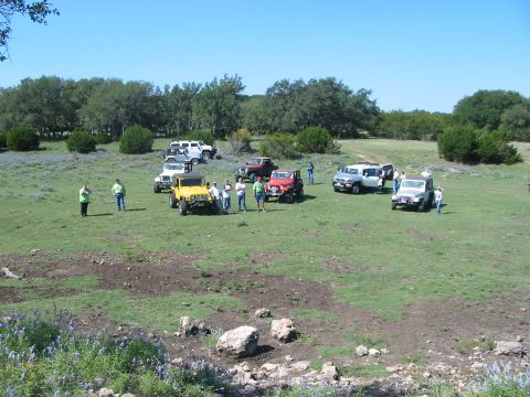 1996 Ford Bronco - A gathering of off-road vehicles and people in a scenic, grassy landscape under a clear blue sky.
