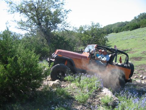 1996 Ford Bronco - An orange Jeep Wrangler kicks up dust as it navigates a , off-road path.