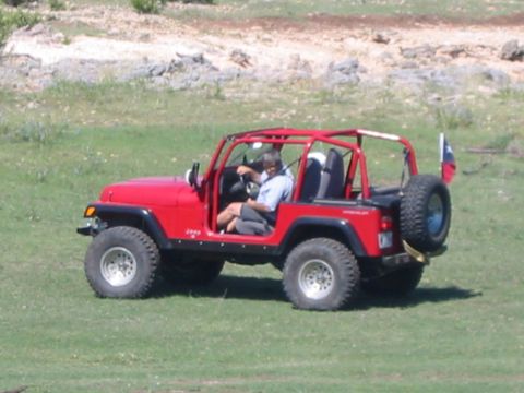 1996 Ford Bronco - A red Jeep Wrangler is parked on a grassy field with a person in the driver's seat.