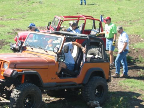 1996 Ford Bronco - Two Jeeps are parked on a grassy, uneven terrain with people around them.