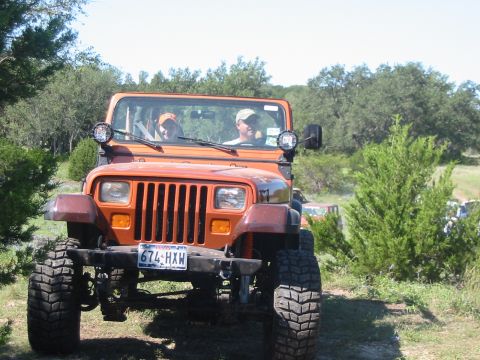 1996 Ford Bronco - An orange Jeep Wrangler is seen from the front, with two occupants visible through the windshield. Another vehicle is partially visible in…