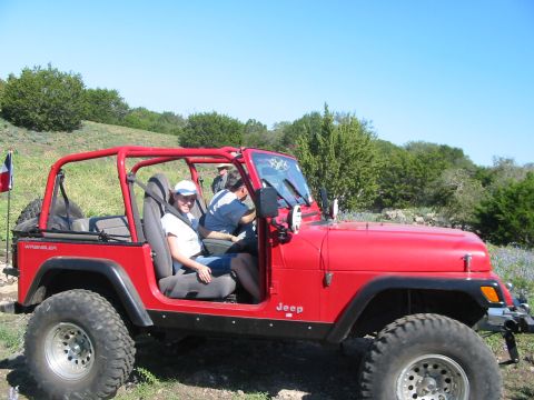 1996 Ford Bronco - A red Jeep Wrangler with a roll cage is parked on a grassy hill under a clear blue sky.