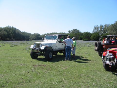 1996 Ford Bronco - A group of people stand around a white Jeep Wrangler Laredo, with other Jeeps visible in the background on a sunny day.