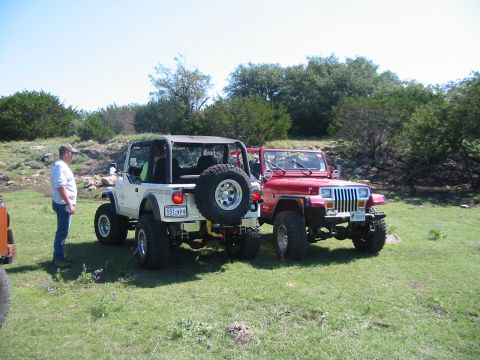 1996 Ford Bronco - Two off-road vehicles are parked side-by-side in a grassy, outdoor area with trees in the background.