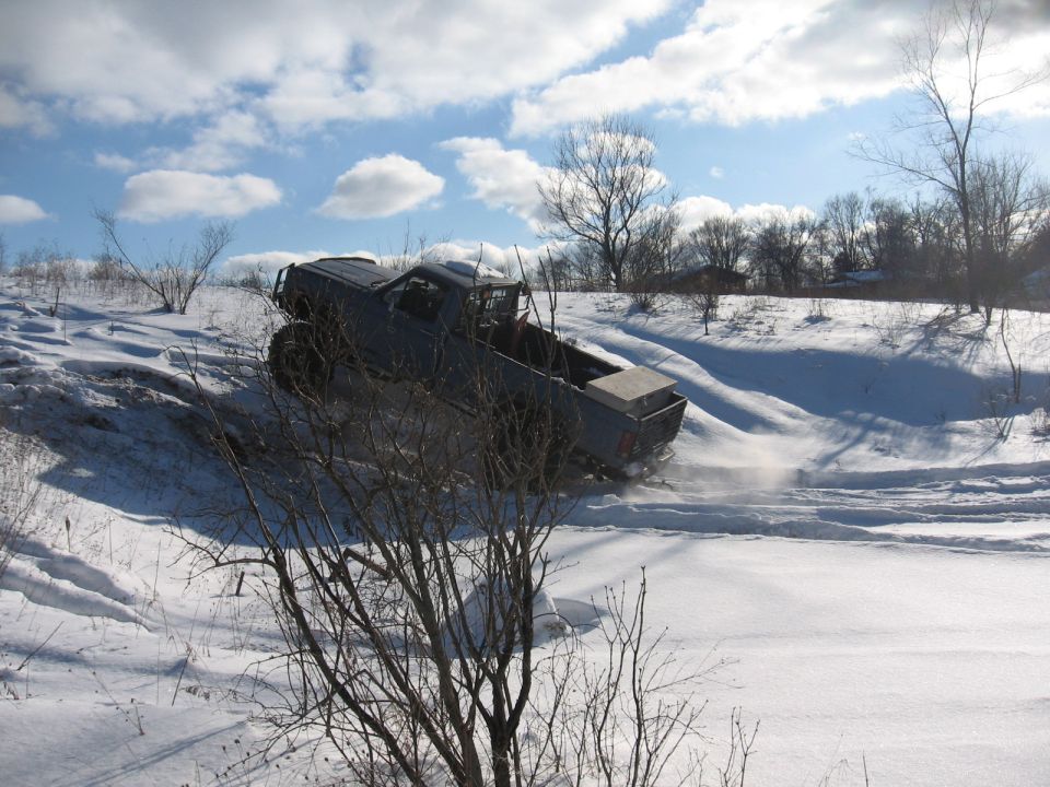Pickup truck with a toolbox in the bed driving up a snowy hill, kicking up snow