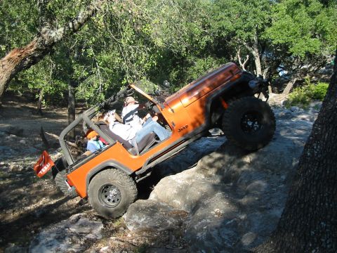 1996 Ford Bronco - An orange Jeep Wrangler navigates a rocky trail with occupants inside.