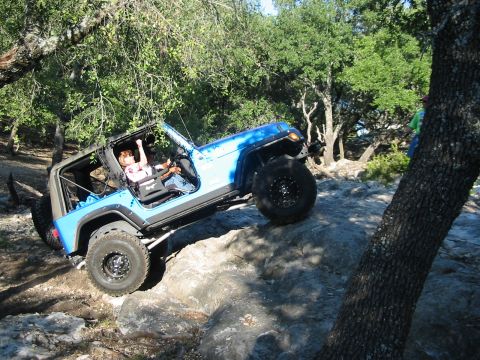 1996 Ford Bronco - A blue Jeep Wrangler navigates a rocky off-road trail with a driver and passenger inside.