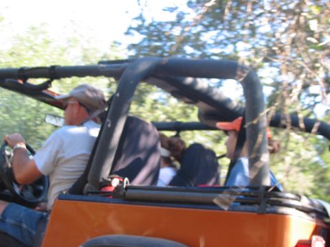 1996 Ford Bronco - People ride in an orange off-road vehicle, possibly a Jeep, on a sunny day.