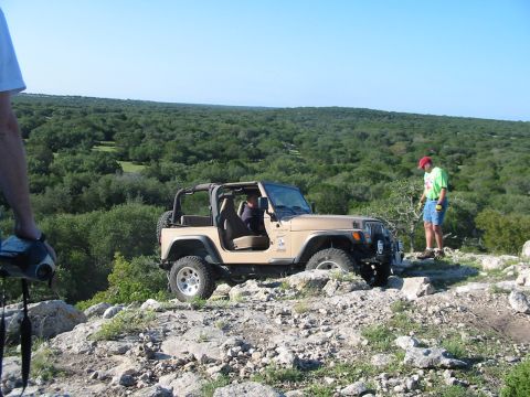 1996 Ford Bronco - A tan Jeep Wrangler navigates a rocky trail under a clear blue sky, with a person observing.