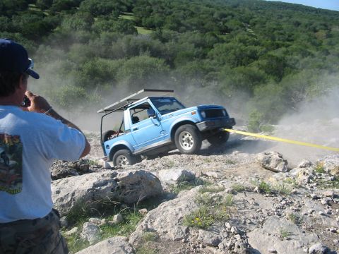 1996 Ford Bronco - A blue off-road vehicle is being towed out of a dusty, rocky area by a yellow strap.