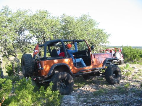 1996 Ford Bronco - Two Jeeps are seen off-roading on a rocky, tree-filled terrain under a bright sky.