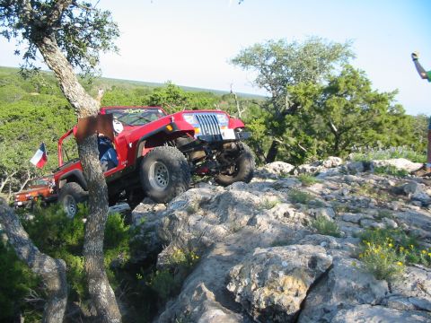 1996 Ford Bronco - A red Jeep Wrangler navigates a rocky off-road trail with a second vehicle in the background.