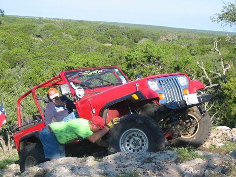 1996 Ford Bronco - A red Jeep Wrangler navigates rocky terrain, with one occupant attending to the front wheel.