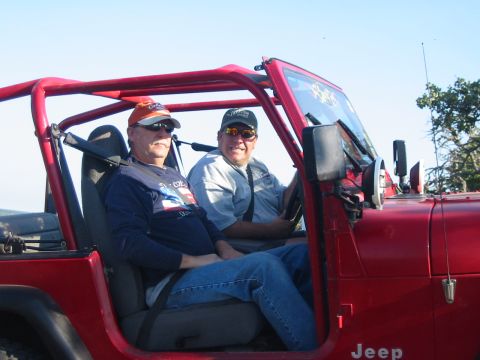 1996 Ford Bronco - Two men are seated inside a red Jeep Wrangler, enjoying a sunny day outdoors.