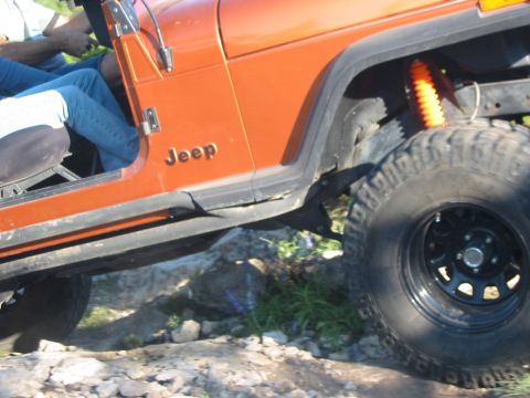 1996 Ford Bronco - Orange Jeep Wrangler navigating rocky terrain, showing its side profile and suspension.