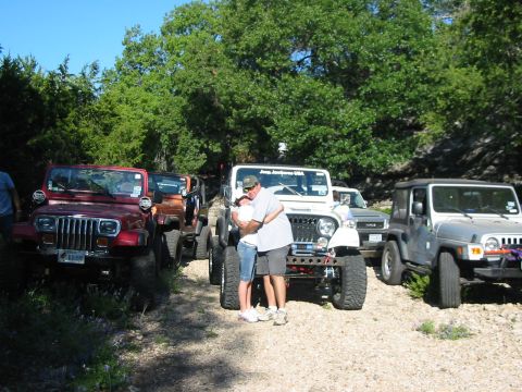 1996 Ford Bronco - Several Jeeps are parked together outdoors, with a couple embracing in front of one of them.