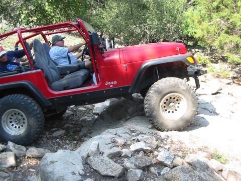 1996 Ford Bronco - A red Jeep Wrangler navigates a rocky trail with two occupants inside.