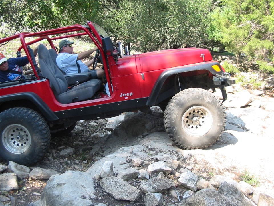 Red Jeep Wrangler side view, off-roading over rocks