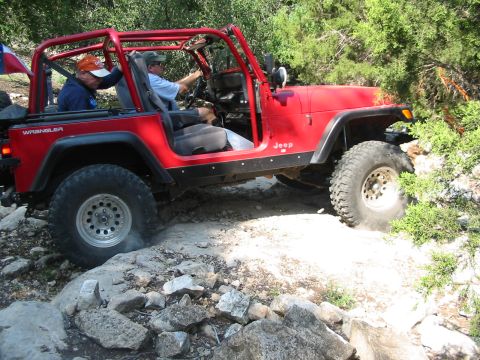 1996 Ford Bronco - This red Jeep Wrangler is navigating a rocky trail with two occupants.