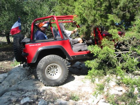 1996 Ford Bronco - A red Jeep Wrangler navigates a rocky trail, with a Texas flag attached to the spare tire.