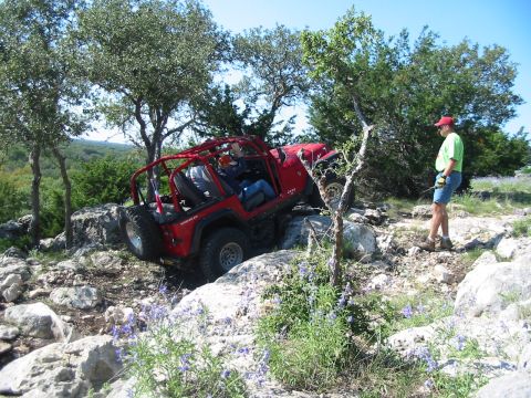 1996 Ford Bronco - A red Jeep Wrangler tackles a challenging off-road course on a sunny day, with a spectator observing the action.