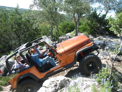 1996 Ford Bronco - A group of people are off-roading in an orange Jeep Wrangler on a rocky trail.