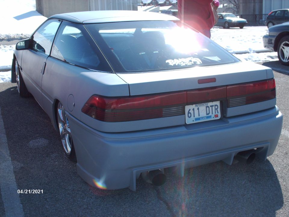 Rear view of light blue coupe with aftermarket body kit and dual exhaust pipes