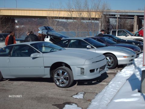 1995 Ford Probe - Several cars are parked in a lot with snow on the ground, including a gray coupe with its doors open.