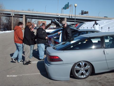 1995 Ford Probe - A group of people stand around several cars, including a gray coupe with chrome wheels.