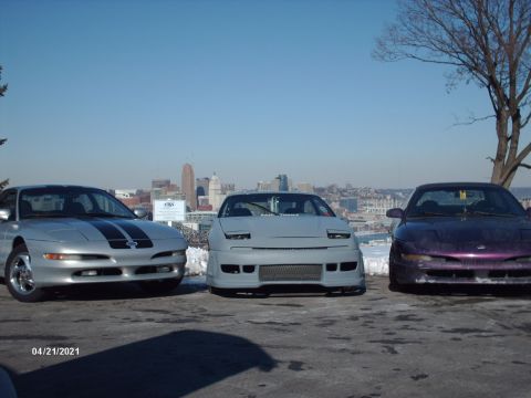 1995 Ford Probe - Three Ford Probes are lined up with a city skyline in the background under a clear blue sky.