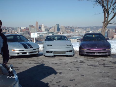 1995 Ford Probe - Three coupes are parked on a snowy overlook with a city skyline in the distance.