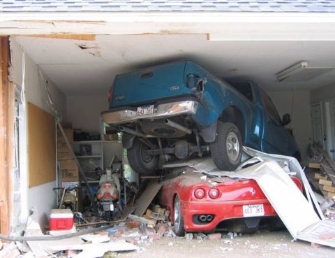 1993 Ford Bronco - A blue Ford pickup truck has crashed into and is resting on top of a red Ferrari in a damaged garage.