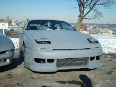 1995 Ford Probe - A gray car with pop-up headlights and an aftermarket body kit is parked outdoors with a city skyline in the distance.