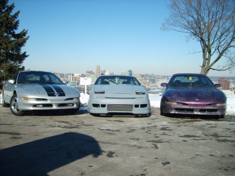 1995 Ford Probe - Three Ford Probes are lined up in front of a city skyline on a clear day.