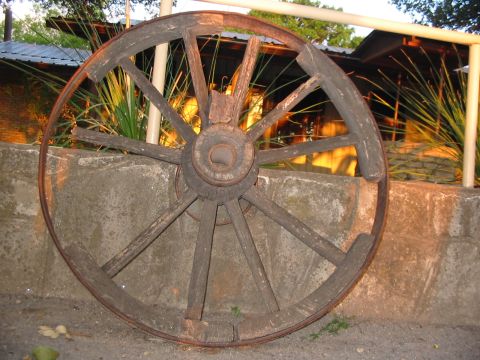 1996 Ford Bronco - This old wooden wagon wheel is leaning against a concrete wall, with a building and vegetation in the background.