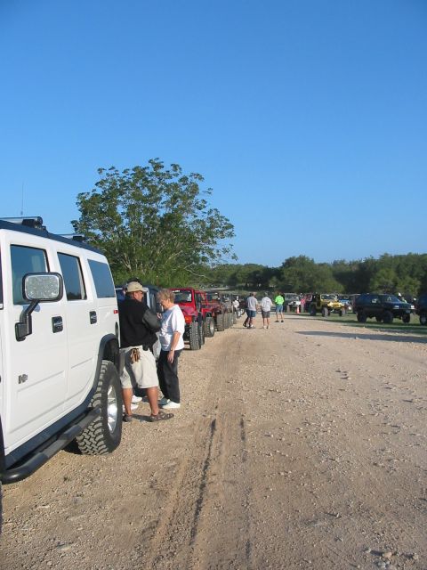1996 Ford Bronco - A group of off-road vehicles are lined up on a dirt road under a clear blue sky.
