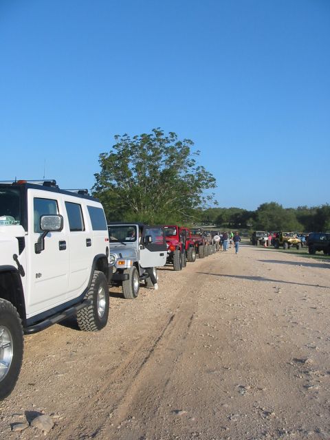 1996 Ford Bronco - A convoy of off-road vehicles, including a white Hummer and several Jeeps, are parked on a dirt path under a clear blue sky.