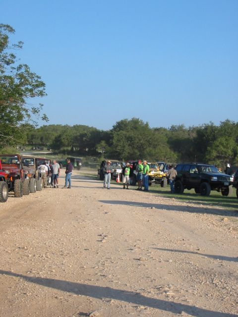 1996 Ford Bronco - A gathering of off-road vehicles and people on a dusty, unpaved road under a clear blue sky.