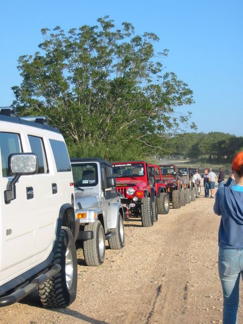 1996 Ford Bronco - A convoy of Jeeps drives down a dusty road, with a large white SUV leading the way.