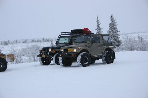 2003 Jeep TJ - A black Jeep TJ and a tan Suzuki Samurai sit parked in a snowy landscape with trees visible in the distance.