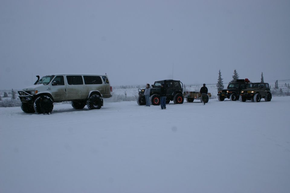 Several modified off-road vehicles, including a van and Jeeps, parked in a snowy landscape