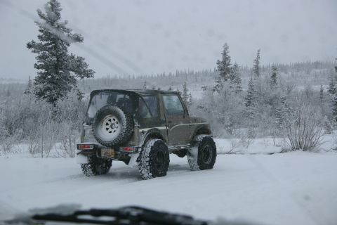 2003 Jeep TJ - A brown Suzuki Samurai navigates a snowy landscape, its spare tire mounted on the rear.