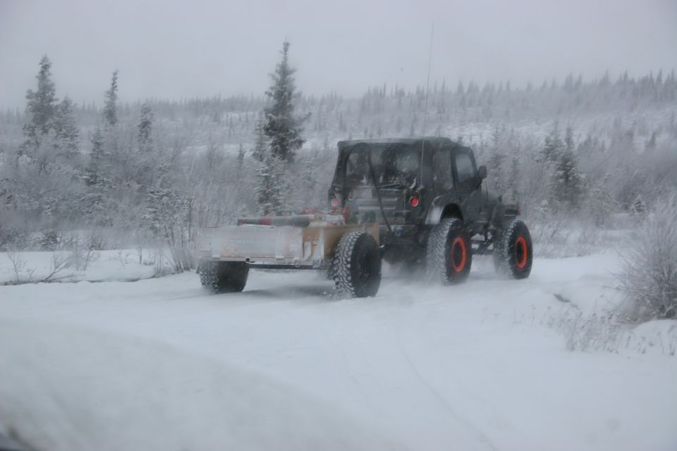 Dark Jeep TJ with trailer driving on a snowy trail, rear view
