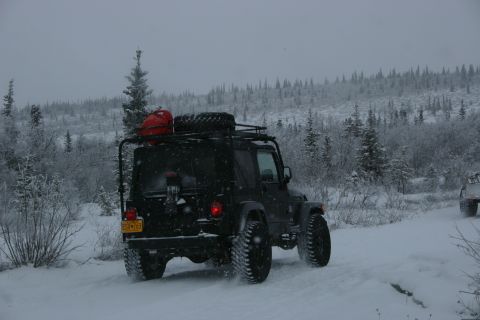 2003 Jeep TJ - A black 2003 Jeep TJ navigates a snowy path through a wooded area.