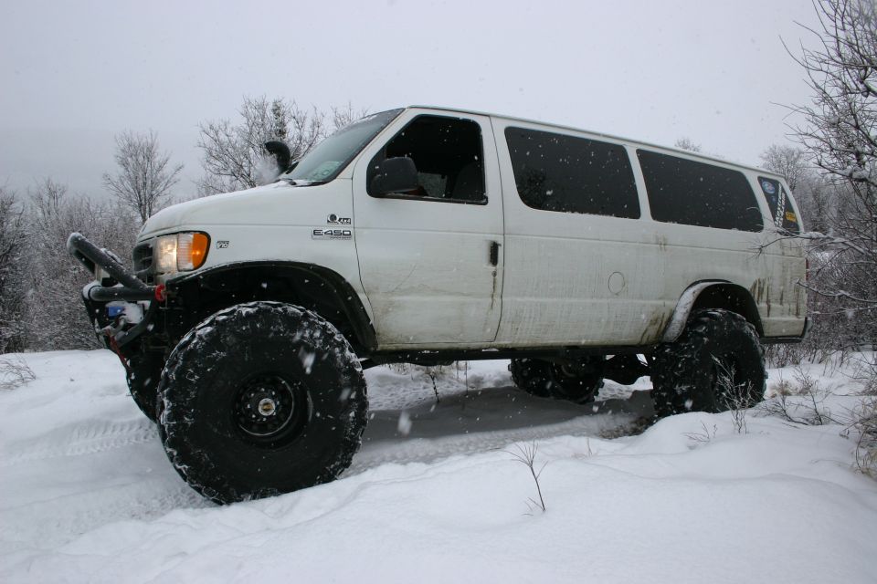 White van with huge tires in snow, snorkel on driver side. E450 badge visible