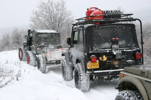 2003 Jeep TJ - Multiple Jeeps navigate a snow-covered trail, one towing a trailer and another equipped with extra fuel and a spare tire.