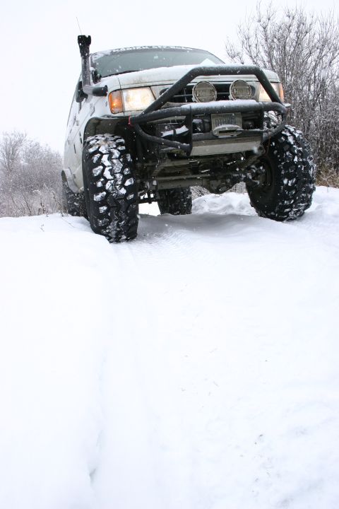 2003 Jeep TJ - A white SUV equipped with a snorkel and bull bar navigates a snowy trail.